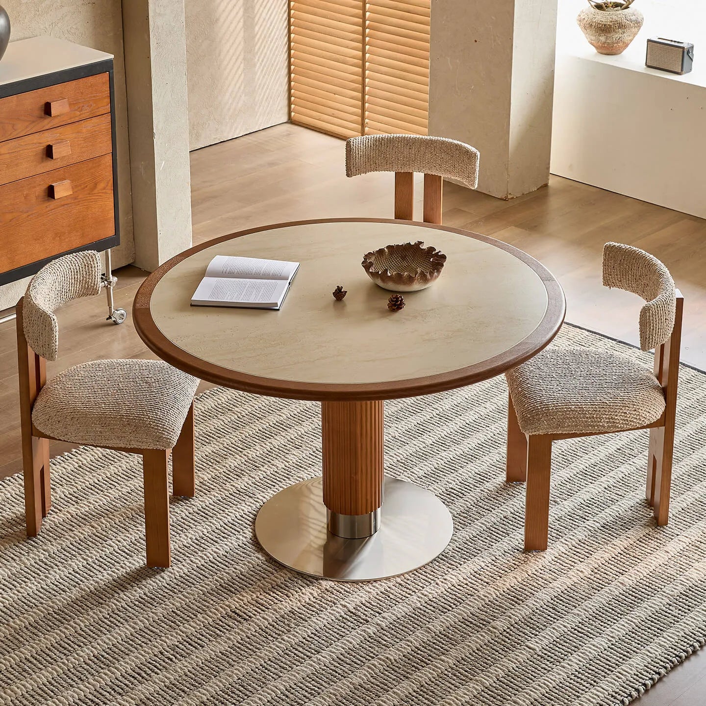Mesa de comedor de piedra sinterizada efecto travertino con base escultórica de fresno y detalle de acero inoxidable